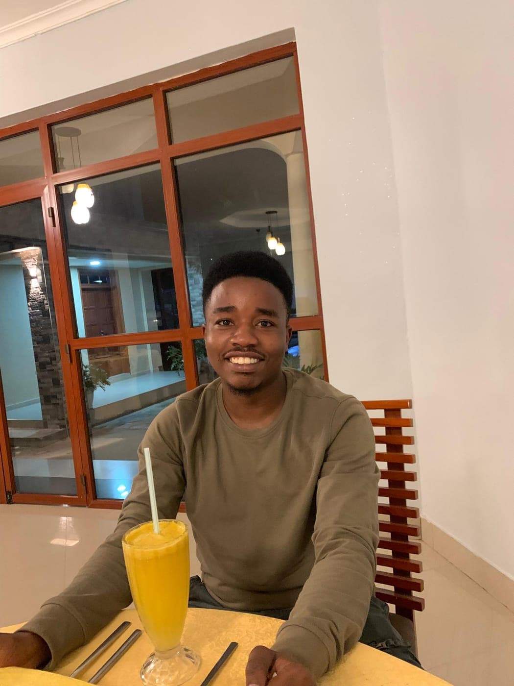 Emmanuel smiling at a table with a glass of juice in the evening